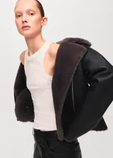 Chaqueta estilo aviador de color negro con interior de piel sintética gris oscuro, cierre frontal cruzado con cremallera y solapas grandes.
