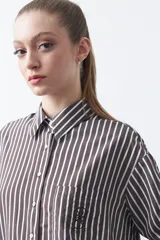 Camisa a rayas verticales blancas y marrones, de manga larga con puños abotonados, cuello camisero y botones frontales. Incluye un bolsillo en el pecho con bordado sutil.
