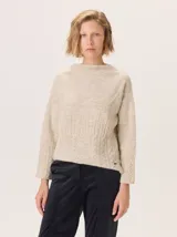Buzo de lana color beige claro, con cuello chimenea y manga larga. Presenta trenzas de punto grueso en el frente y en los puños, con un diseño texturizado que se asemeja a espigas o ramas.