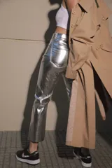 Pantalón de ecocuero metalizado color plateado, de corte capri semi oxford y tiro medio-alto. Presenta cierre frontal con botón metálico y costura horizontal a la altura de la rodilla.