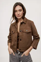 Campera negra de efecto gamuzado con cuello camisero, cierre frontal de botones, bolsillos plaqué en el pecho y detalles de costuras decorativas y calados.