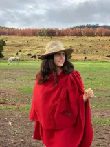 Capa roja de lana con apliques de cuero en los hombros y en el borde de la abertura frontal.