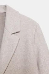 Abrigo de paño con cuello de solapa, manga larga y cierre frontal con un botón. Diseño de corte recto y minimalista.