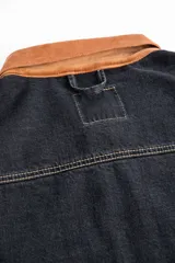 Campera corta de jean negro con cuello de pana marrón, confeccionada en jean grueso 100% algodón de 14 onzas, con costuras marrones en contraste.