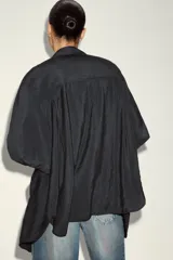 Camisa de corte amplio y fluido con cuello solapa, manga larga con puños abotonados y bolsillo de plastrón en el delantero. Presenta cierre frontal con botones y un acabado satinado.