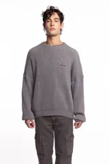 Buzo de punto inglés grueso en color gris melange, de corte amplio con hombros caídos y mangas largas, con sutil bordado de la marca en el pecho.