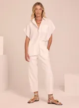 Camisa blanca de lino con cuello clásico, manga corta amplia, cierre frontal con botones y bolsillo de parche en el pecho.