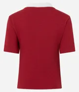 Blusa tipo polo de manga corta, color rojo, con cuello y escote en V con bies blanco contrastante. Presenta una textura gofrada y un bordado pequeño en el pecho con el texto "LE SPORT Paris".