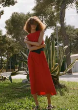 Vestido midi de corte evasé en color rojo, con cuello redondo, sin mangas y tirantes anchos. Presenta un diseño con pinzas en la cintura y cierre posterior con cremallera y botón.