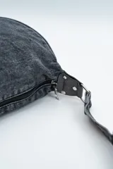 Cartera tipo bandolera de denim color negro, con diseño de media luna y correa ajustable.