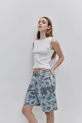 Bermuda de jean de calce amplio y largo a la rodilla, con estampado floral oscuro sobre fondo de mezclilla celeste. Cuenta con cinco bolsillos, trabillas para cinto y cierre frontal con botón y cremallera.