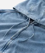 Campera tipo bomber confeccionada en tejido de jean, con cierre frontal de cremallera, capucha ajustable con cordones y bolsillos frontales. Presenta puños y cintura elásticos, ofreciendo un ajuste cómodo y un estilo urbano.