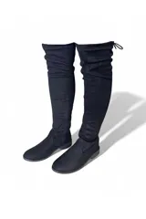 Bota bucanera de gamuza marrón, de caña alta elástica por encima de la rodilla, punta redondeada, suela plana y cierre lateral interno.