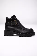 Bota corta tipo borcego de cuero negro con textura granulada, suela track dentada y tira decorativa con hebilla metálica en el tobillo.