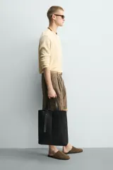 Bolso tipo shopper de diseño minimalista en color negro, con estructura vertical, doble asa de hombro y detalle de tira decorativa frontal con cierre magnético.