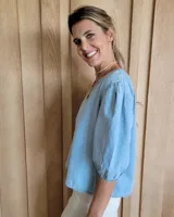 Blusa celeste de mangas 3/4 abullonadas, escote en V con detalle de bordado y lazo decorativo.