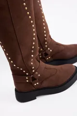 Bota de caña alta confeccionada en cuero vacuno, color negro, con diseño de tachas metálicas dispuestas en forma de arco a lo largo de la caña y correa decorativa con hebilla en la zona del tobillo. Presenta suela track de goma robusta.