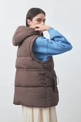 Chaleco puffer negro con diseño acolchado, capucha desmontable y cierre frontal. Cuenta con cordones ajustables en la cintura y bolsillos laterales.
