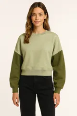 Buzo de tejido de punto color verde oliva, con diseño de bloques de color: cuerpo principal verde claro y mangas verde oscuro. Presenta cuello redondo y puños y cintura acanalados.