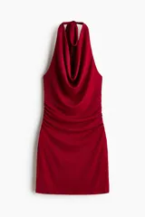Vestido corto rojo de punto elástico, con escote halter drapeado y tirantes anchos para anudar al cuello. Diseño entallado con costuras fruncidas en los laterales de la cintura.