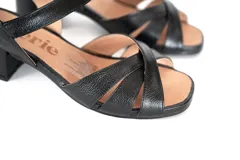 Sandalias de cuero negro con tiras cruzadas en la parte delantera y tira ajustable en el talón. Cuenta con taco bloque bajo y suela flexible.