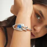 Pulsera semirrígida de aleación de metales bañada en plata, con diseño de eslabón central y cristal facetado de corte rectangular en color azul.