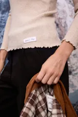 Polera de tejido de punto fino color blanco, con cuello alto, mangas largas y terminaciones con detalle de ondas en puños, cuello y ruedo.