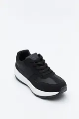 Zapatilla urbana de diseño contemporáneo con capellada que combina paneles de diferentes texturas en color negro, ajuste con cordones y suela robusta de color blanco.