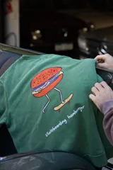 Buzo verde con estampa de hamburguesa andando en skate y texto "skateboarding hamburger".