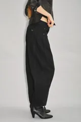 Jean de tiro medio-alto, color negro, de calce holgado con piernas anchas que se estrechan hacia el tobillo. Presenta pinzas en las rodillas que acentúan su forma "balloon" y un recorte lateral. Confeccionado en denim rígido con lavado suavizado, cierre y botón.