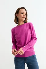 Sweater de punto liso color fucsia, con cuello redondo y mangas largas terminadas en puños con tres botones decorativos.