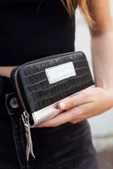 Billetera mediana de cuero negro con textura croco y detalles plateados. Tiene cierre y logo de la marca en el frente.