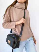 Bandolera de cuero negro con textura grabada tipo cocodrilo en el frente y laterales lisos. Cuenta con doble compartimento con cierre metálico, correa larga ajustable y etiqueta de cuero natural con logo grabado.