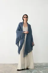 Ruana triangular tejida en lana merino extrafina, lino y viscosa, con textura aireada y terminación de flecos en los bordes. Diseño versátil y envolvente.