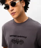 Remera gris oscuro de algodón, con cuello redondo y mangas cortas. Presenta un estampado frontal localizado con la inscripción "Avenged Sevenfold" y una calavera con alas.