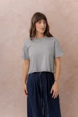 Remera blanca de corte crop y calce relajado, con cuello redondo y mangas corta terminadas con delicados volados, al igual que el ruedo.