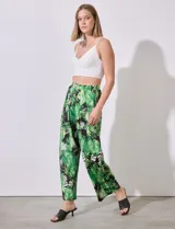 Pantalón largo de seda fría estampada con hojas de palmera en tonos verdes y blancos sobre fondo negro. Tiene pretina ancha elastizada.