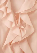 Blusa de seda color rosa pálido con volados frontales, cuello redondo y mangas largas con puños elásticos.