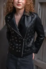 Campera de eco cuero negro con solapas anchas, cierre diagonal metálico y detalle de múltiples ojalillos metálicos distribuidos en el frente y las mangas.