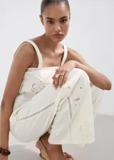 Pantalón palazzo color blanco con detalles bordados en el bajo de las piernas, tiro medio y cintura elástica con cordón ajustable.
