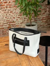 Bolso tote grande de cuero color crudo con detalles en negro, cierre superior y doble asa de hombro.