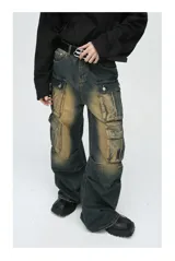 Pantalón de jean ancho (baggy) con lavado oscuro y efecto desgastado en tonos marrones/ocre. Presenta múltiples bolsillos cargo grandes con tapa y botones a presión en las piernas.