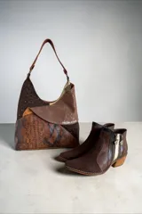 Cartera de cuero de diseño envolvente y líneas orgánicas, con combinación de texturas, apliques y estampado de serpiente, asa de hombro y bolsillos exteriores.