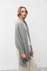 Chal abierto de tejido de punto en color gris, con textura suave y etiqueta de cuero sintético en el borde inferior.