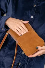 Bolso tipo pocket bag confeccionado en cuero vacuno con frente de pelo natural estampado con manchas blancas. Cuenta con cierre superior, bolsillo frontal con detalle de bordado metálico de flor de lis y correa de cuero desmontable.