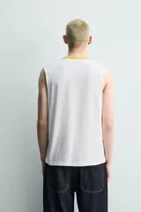 Musculosa de corte relajado color blanco, con cuello redondo en contraste color amarillo. Presenta estampado frontal con texto en color negro.