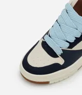 Championes casuales de estilo urbano con diseño de paneles en colores azul marino, beige y celeste. Presentan suela tipo caja de goma color crema con base marrón, cordones gruesos en color celeste y lengüeta acolchada.