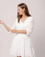 Vestido corto blanco de broderie 100% algodón con escote en V y mangas tres cuartos. Presenta elástico en la cintura, falda corte A y volado en el ruedo.