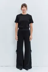 Pantalon negro de corte amplio y tiro alto, confeccionado en tejido con sutil acabado brillante. Presenta un diseño con cordones laterales ajustables a lo largo de las piernas.
