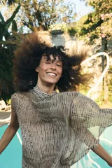 Blusa de cuello subido y manga sisa, confeccionada en tejido fluido semitransparente con estampado de lunares en tonos beige y negro. Presenta un diseño superpuesto tipo capa con caída asimétrica y cierre posterior con abertura y botón.